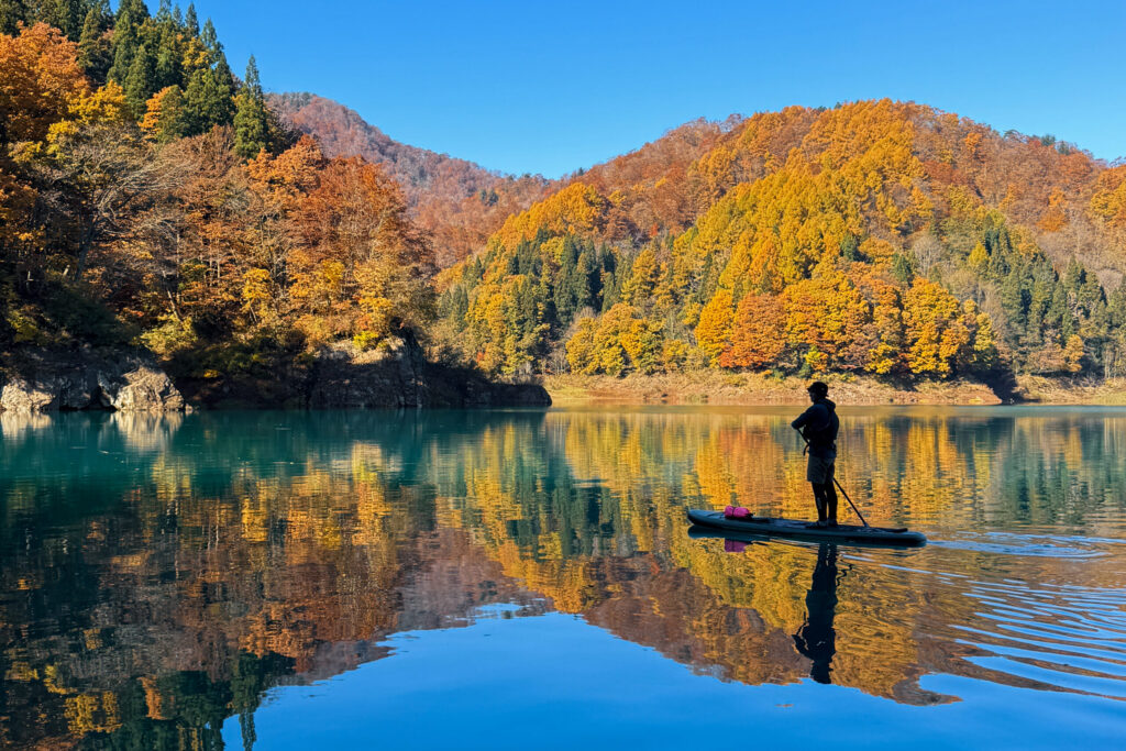 紅葉の山々が映る田沢湖でSUP（サップ）に立つ参加者