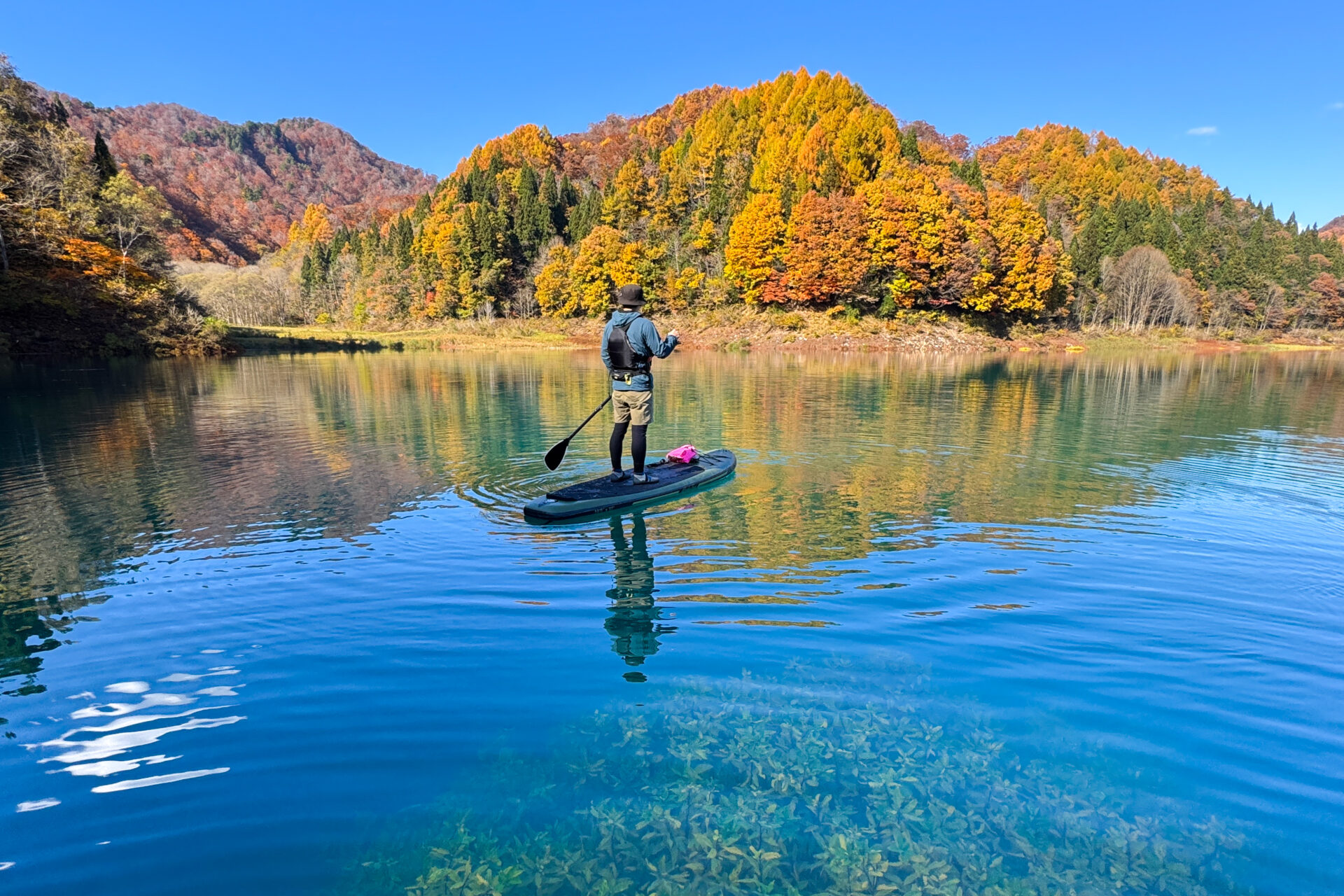 紅葉に染まる山々を背景に田沢湖でSUPに乗る参加者