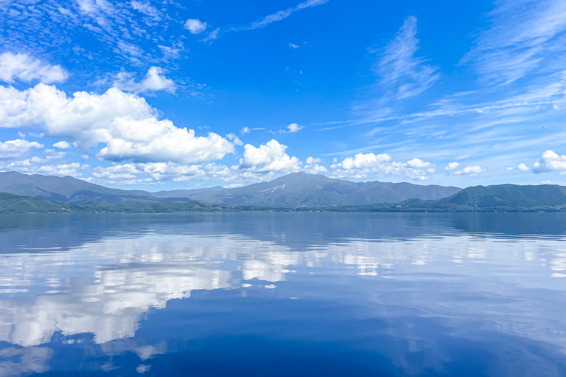 風のない朝、向かいの山が映り込む田沢湖の水面