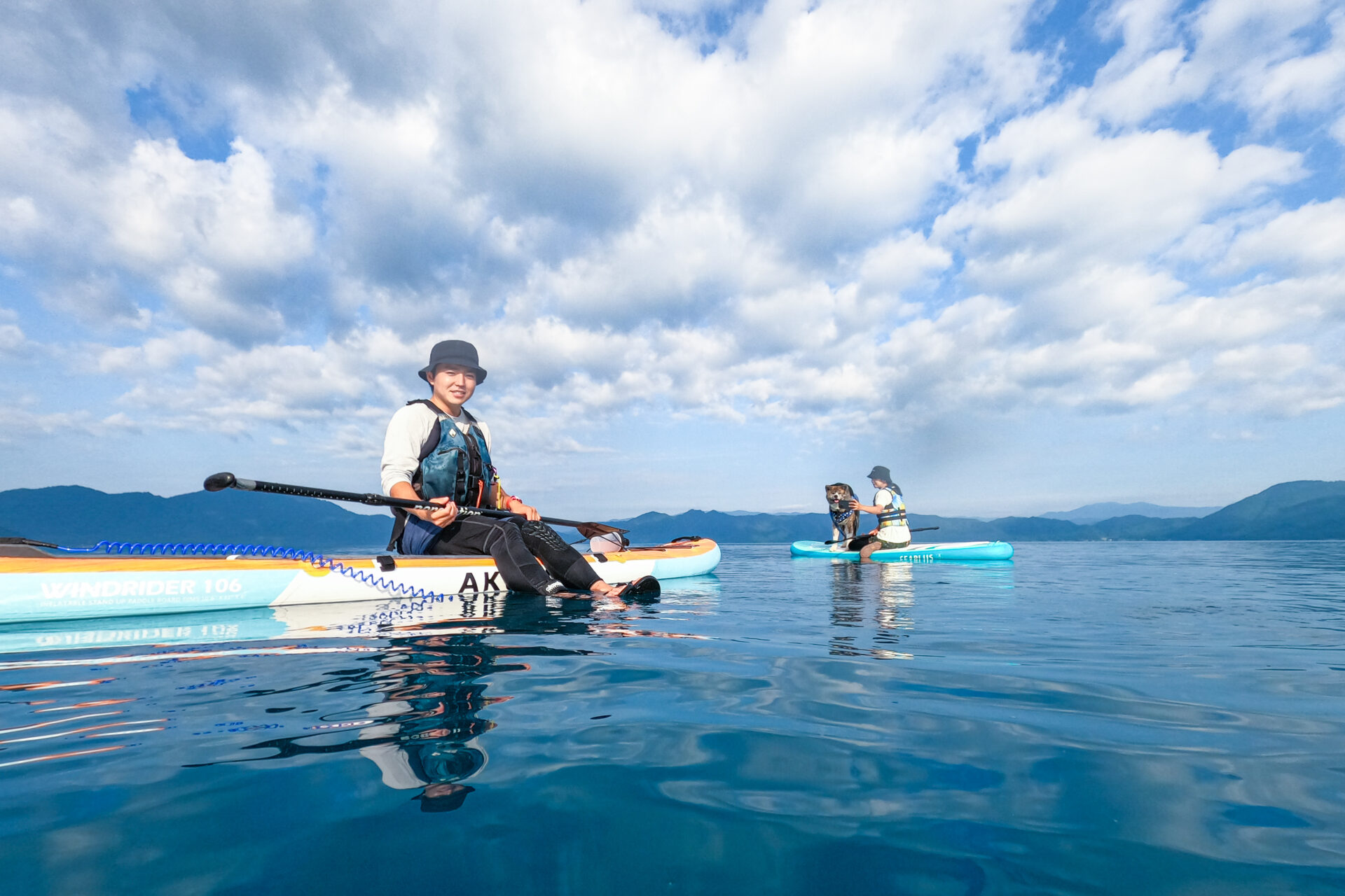 青空が広がる田沢湖で、日中のSUPツアーを楽しむガイドと秋田犬