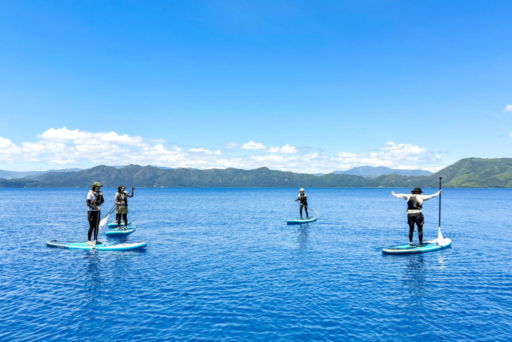 青空の下、田沢湖ブルーの湖面でSUPを楽しむツアー参加者たち