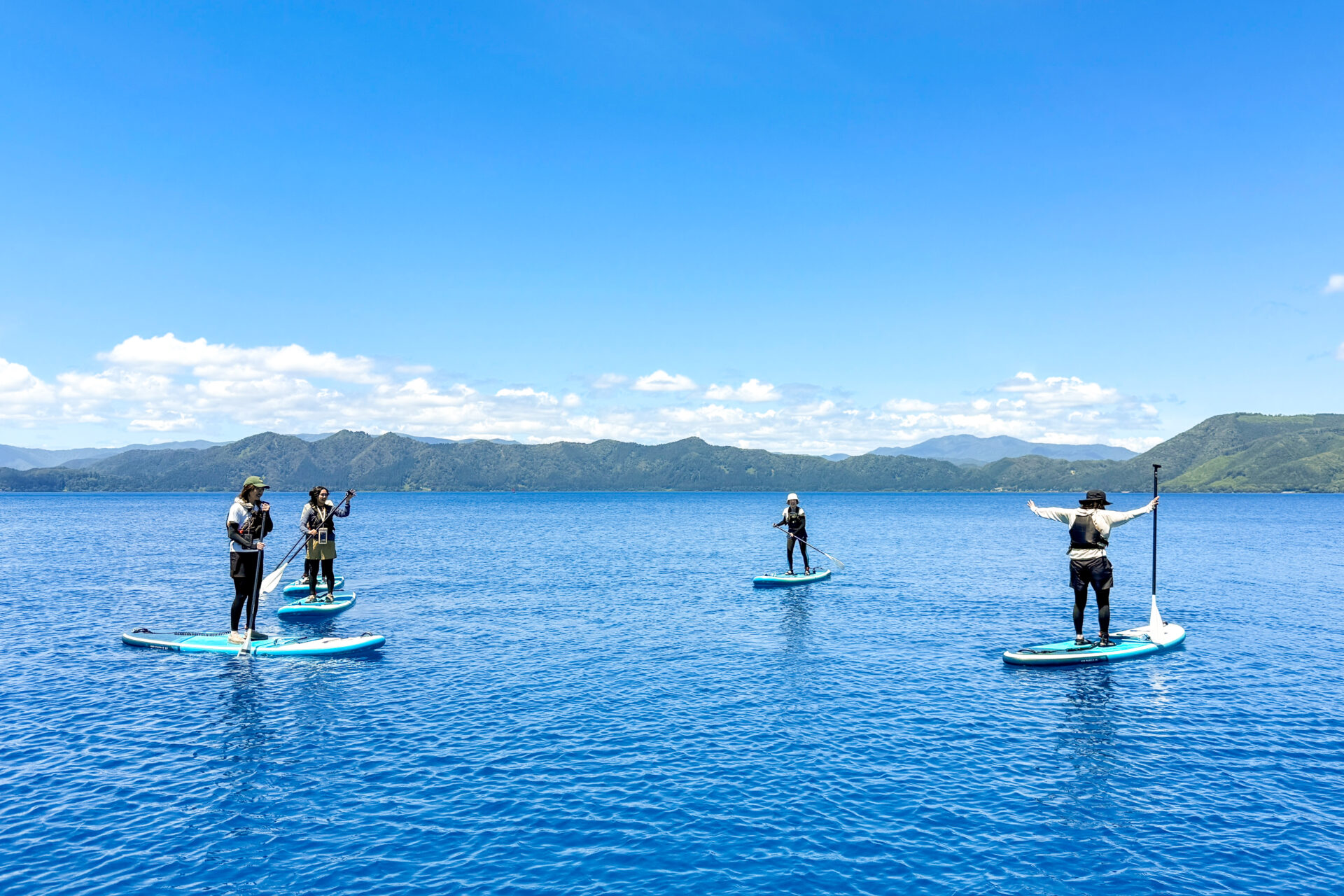 青空の下、田沢湖ブルーの湖面でSUPを楽しむツアー参加者たち