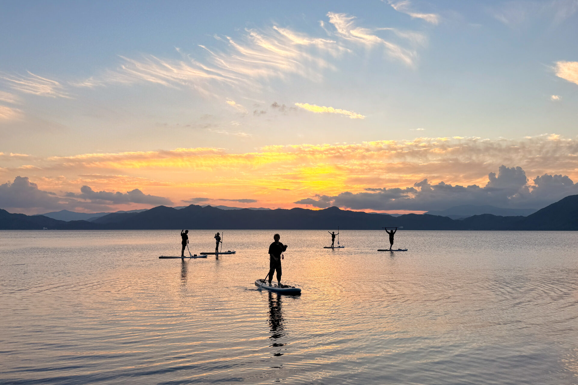 夕焼けに染まる田沢湖で、サンセットSUPを楽しむ参加者たちのシルエット